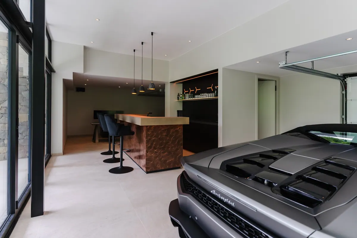 Bar met barkrukken in de garage, op de voorgrond een sportwagen