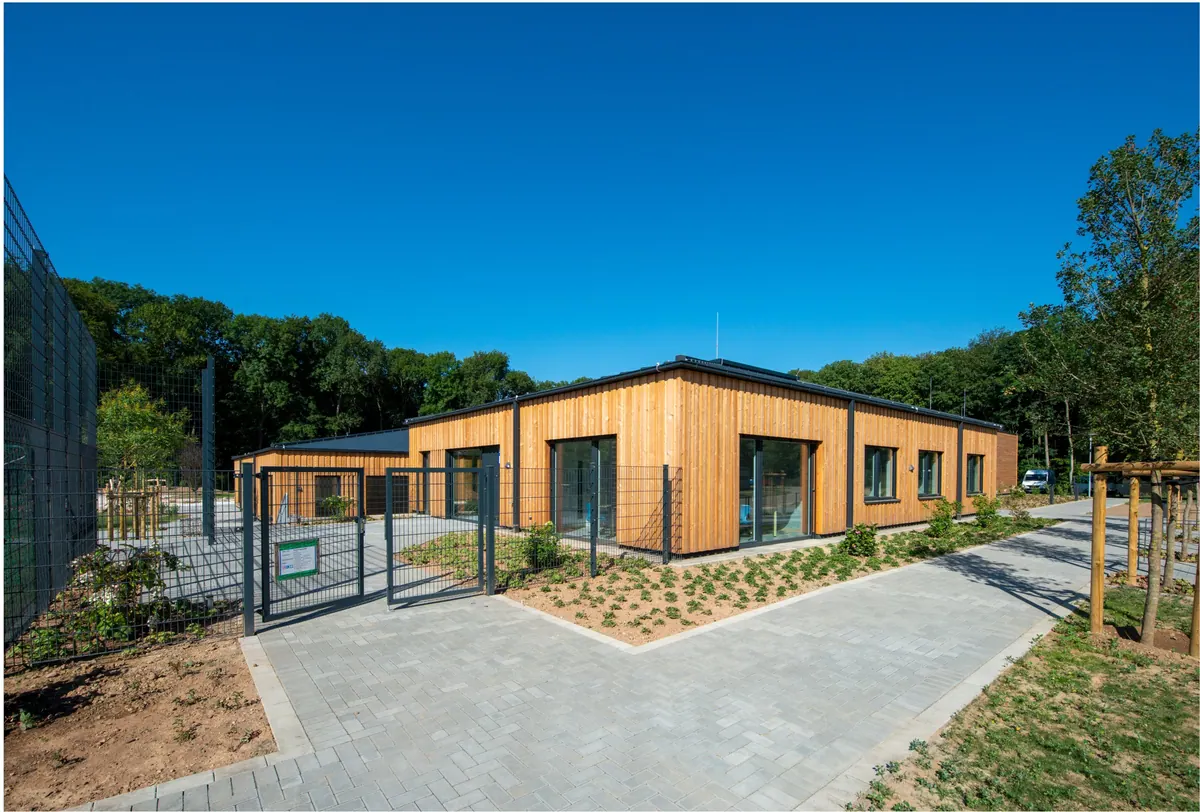 Kita am Forschungszentrum Jülich mit Holzfassade, flach geneigten Dächern und Eingangstor unter blauem Himmel