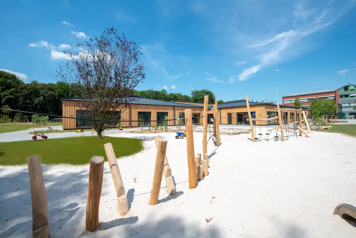 Sandspielplatz mit Holzpfählen und Kletterelementen vor dem Gebäude