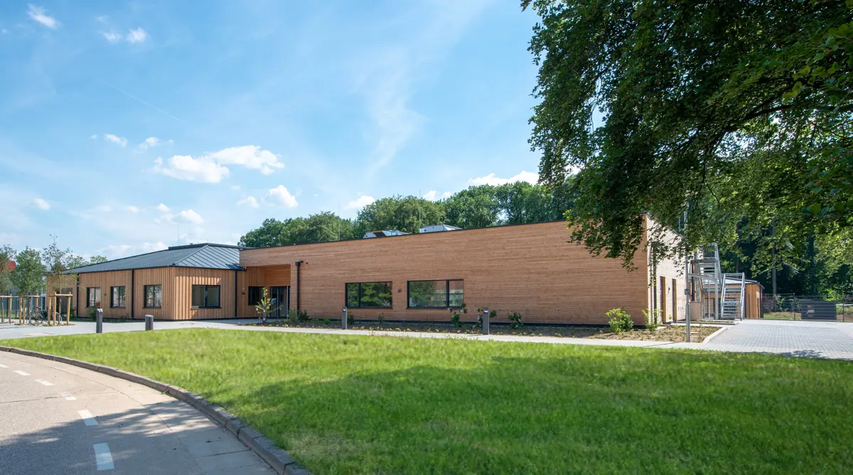 Kita-Gebäude am Rand einer Wiese mit altem Baumbestand