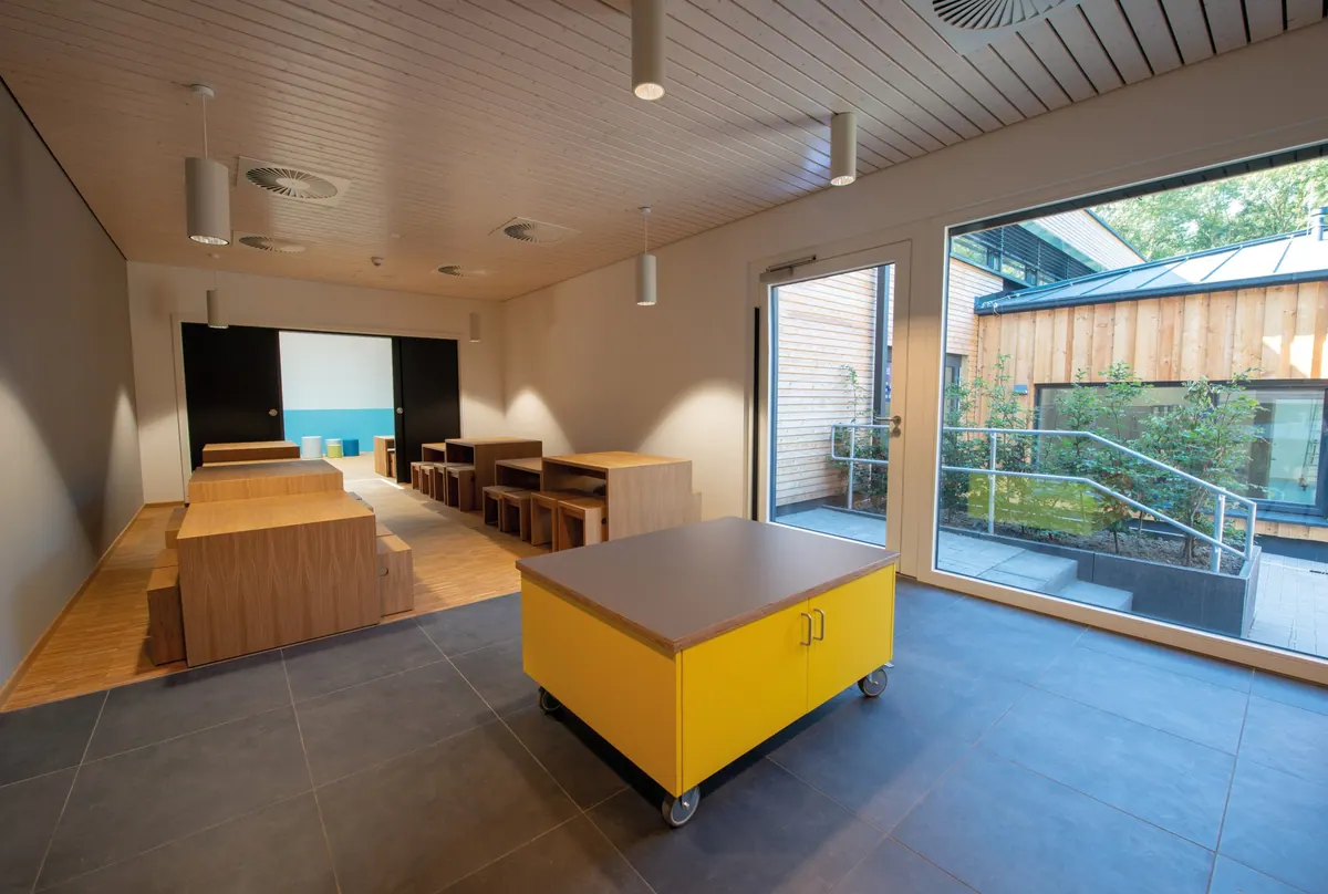 Gruppenraum mit Holzdecke, gelbem Spieltisch und Fenster zur Terrasse