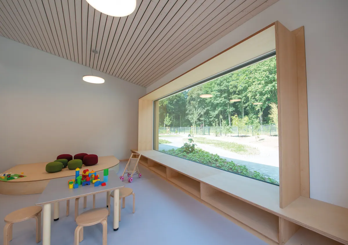 Gruppenraum mit Sitzfenster aus Holz, Kindertischen und Blick ins Grüne