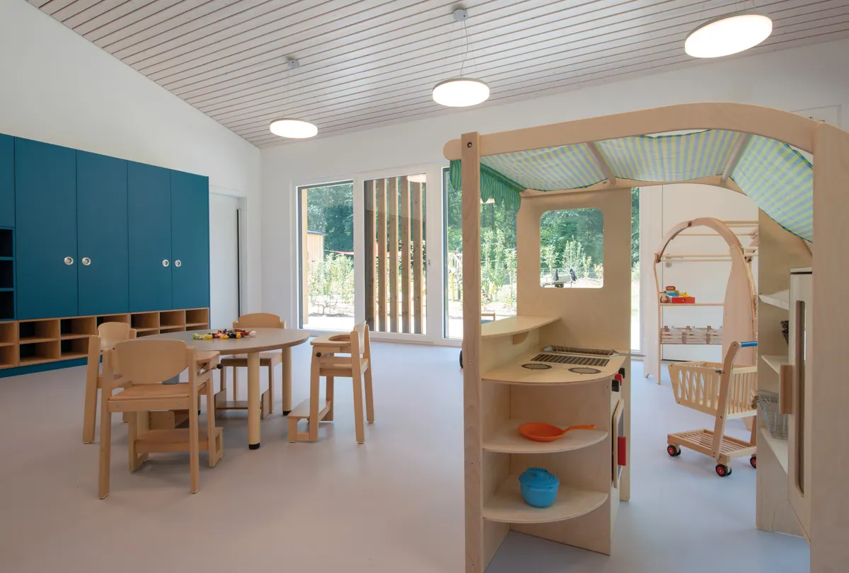 Gruppenraum mit Spielküche, Holzhaus-Einbau und blauen Schränken