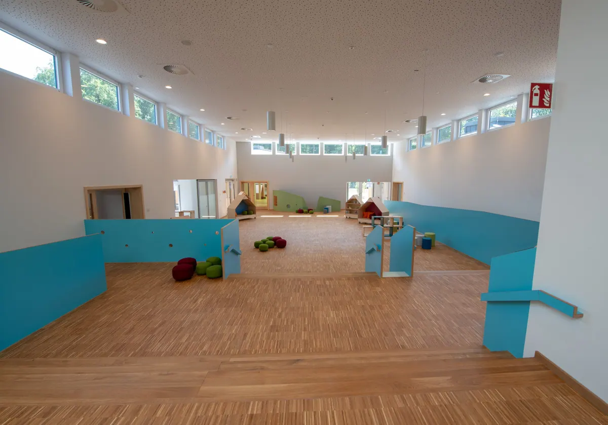 Turnhalle der Kita mit Holzboden, türkisfarbenen Wandpolstern und Fensterband