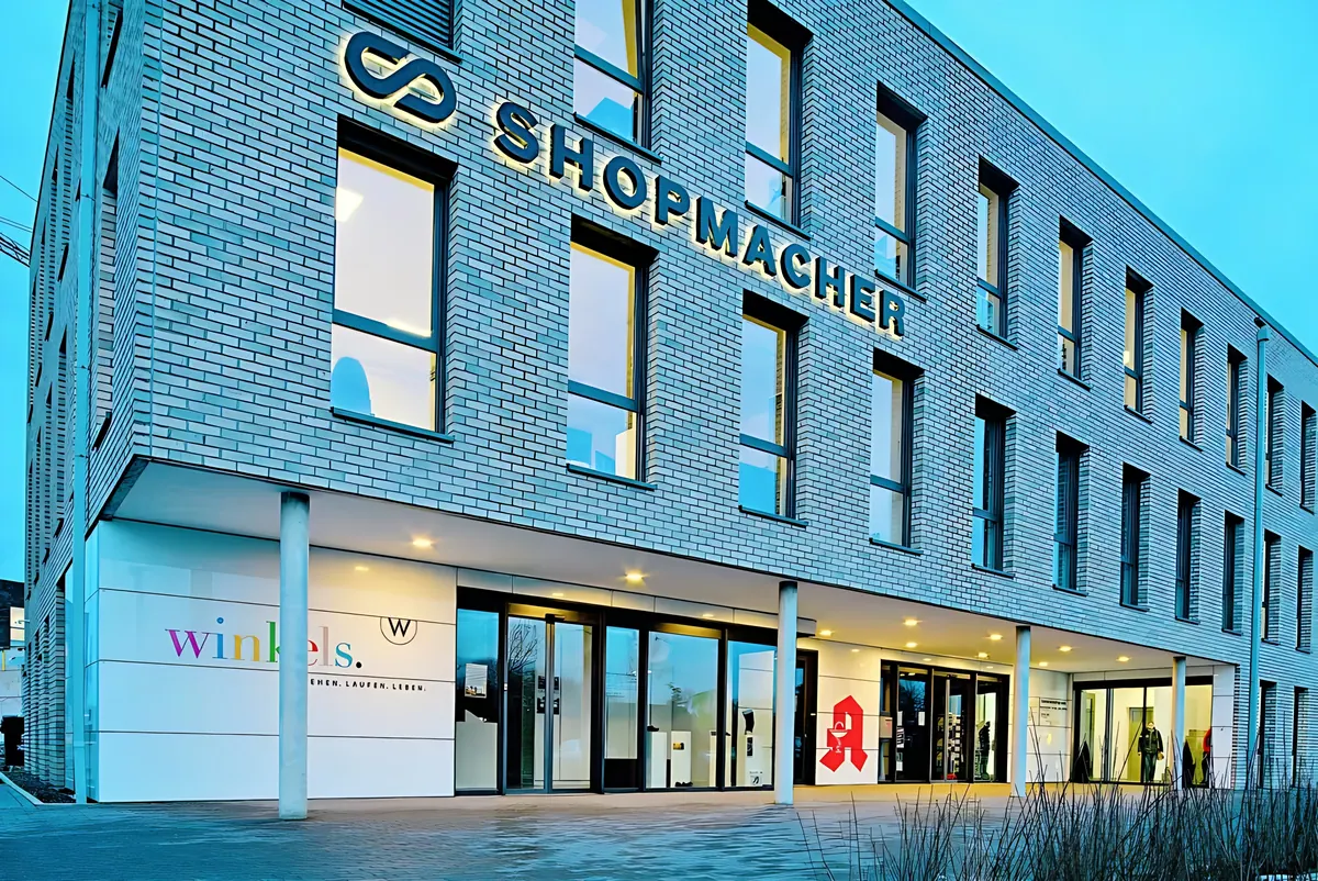 Überdachter Eingangsbereich im Erdgeschoss am Abend mit beleuchteten Ladenflächen