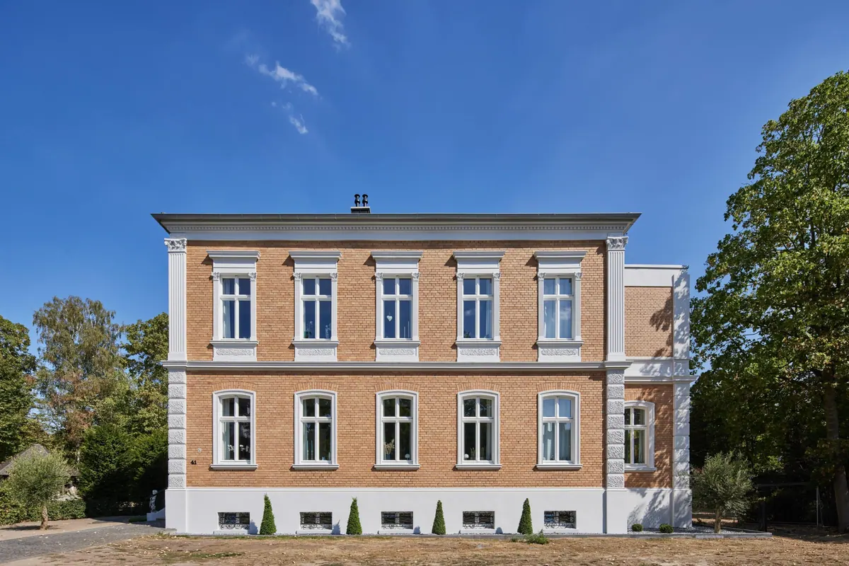 Zijaanzicht van de villa met gerestaureerde gevel en oude bomen