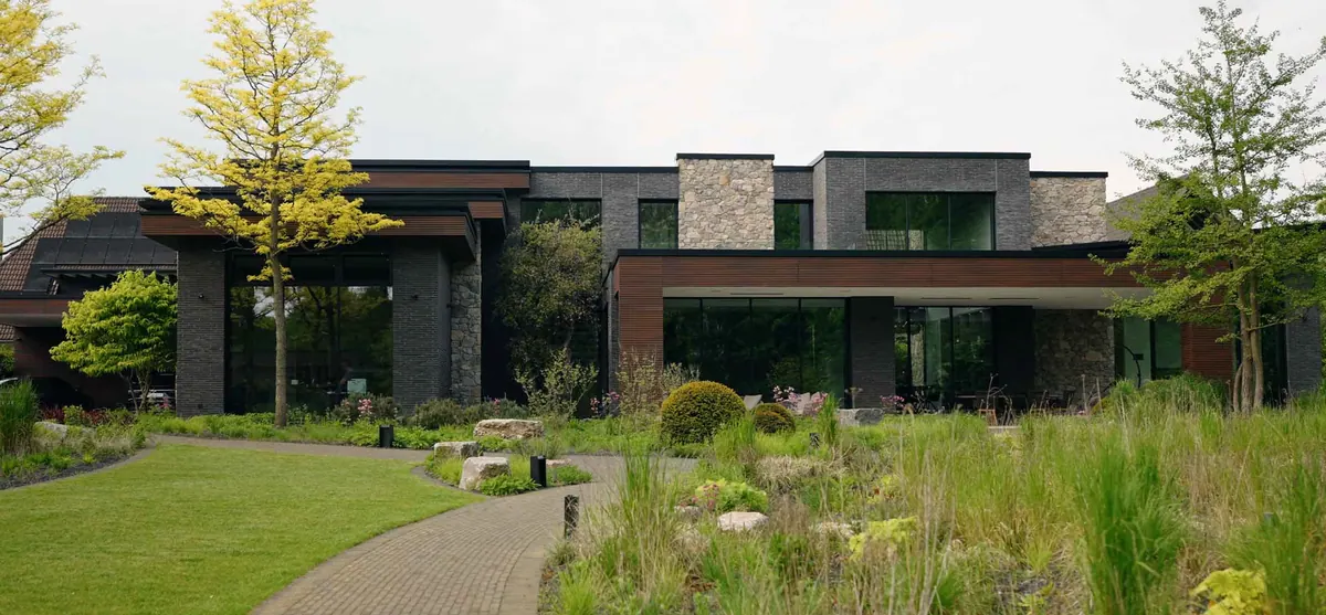Moderne woning met donkere baksteen, natuursteen en hout achter een natuurlijk beplante tuin